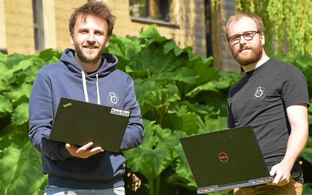 Photo de Léo Richer et Christophe Hauquiert debout avec leur ordinateur entre les mains.