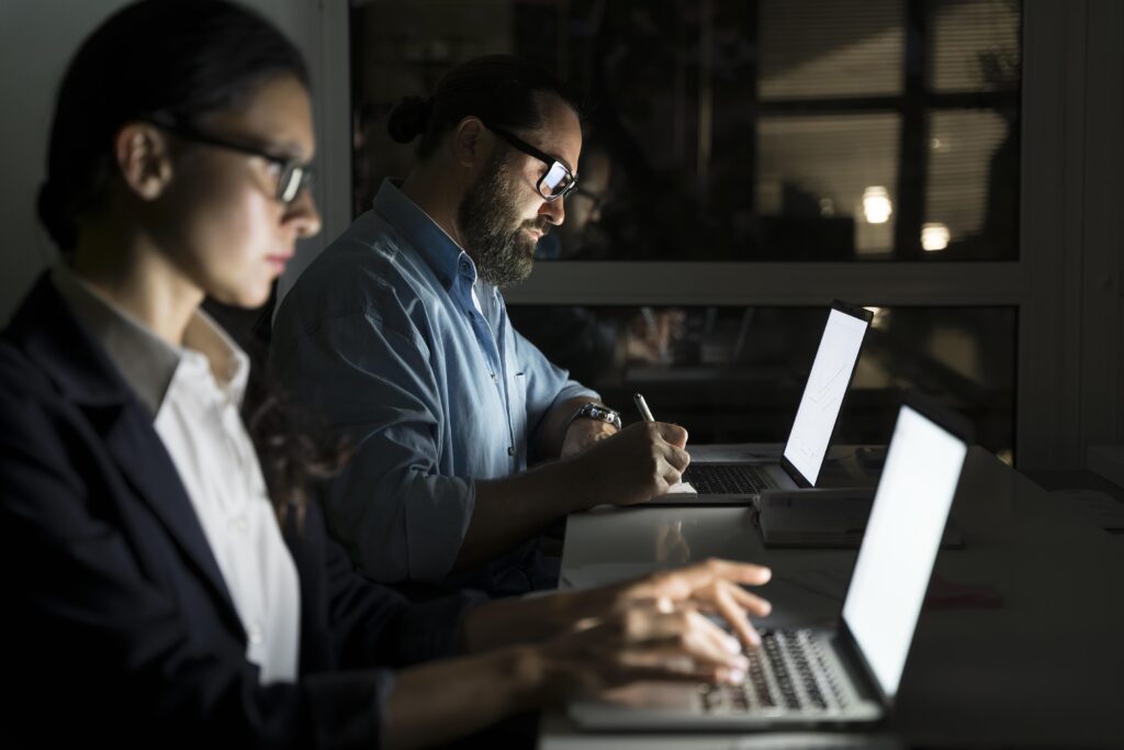 Deux collègues concentrés, travaillant tard sur leurs ordinateurs portables dans un bureau