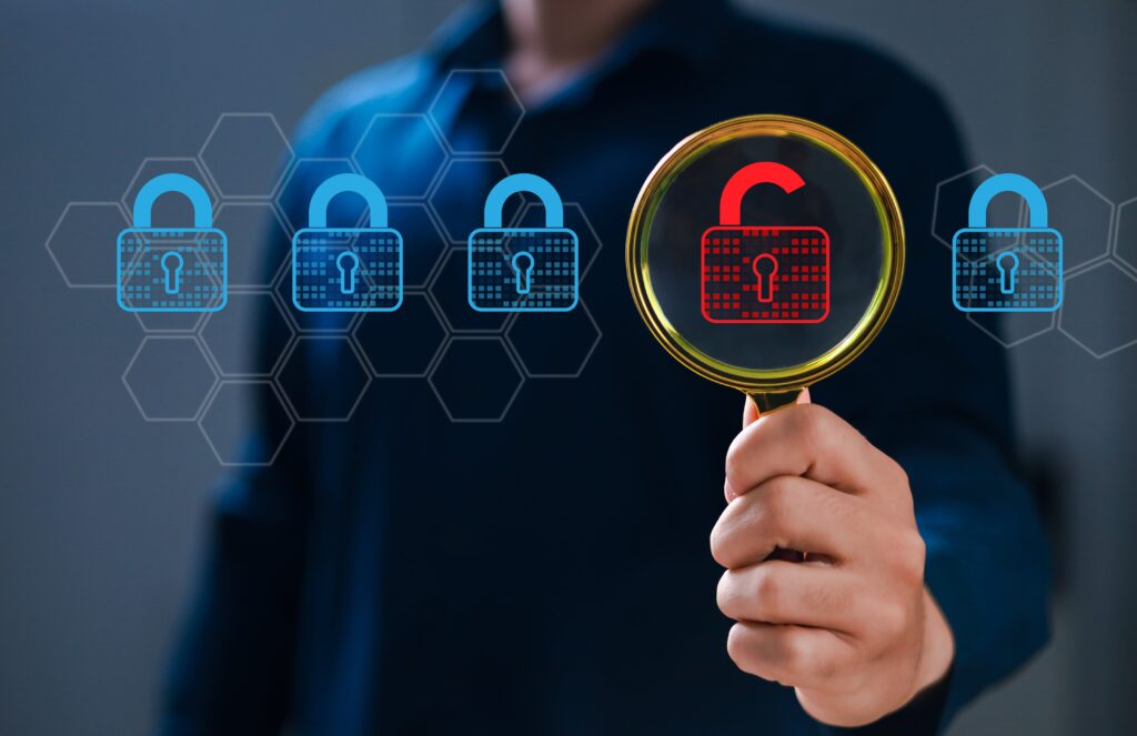 Main tenant une loupe sur un cadenas rouge déverrouillé, symbolisant l’identification d’une vulnérabilité au sein d’un système sécurisé représenté par plusieurs cadenas bleus