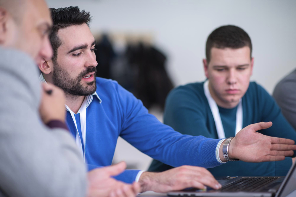 Trois hommes jeunes en réunion regardent ce que l'un d'eux pointe sur un écran