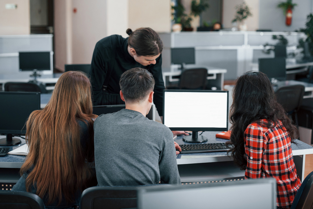 Un conseil en cybersécurité forme des collaborateurs aux principales menaces. Ils sont trois devant un ordinateur et le formateur les regarde debout au dessus